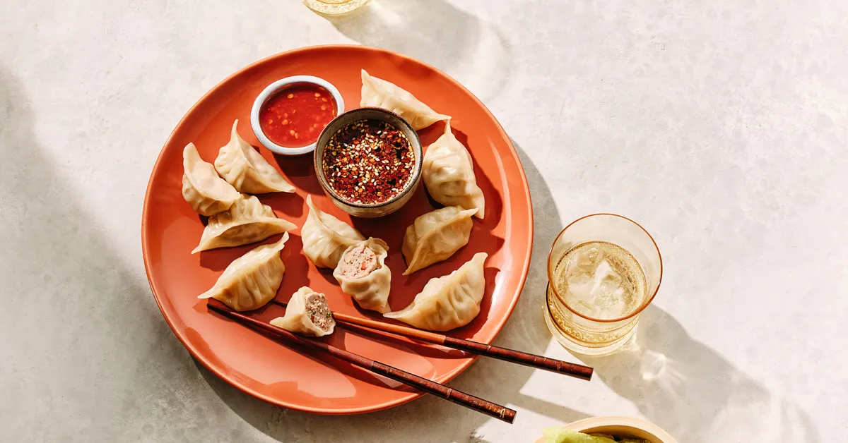 Plate of pork dumplings with dipping sauces and chopsticks, served alongside a beverage, highlighting pork’s versatility and global flavor appeal.